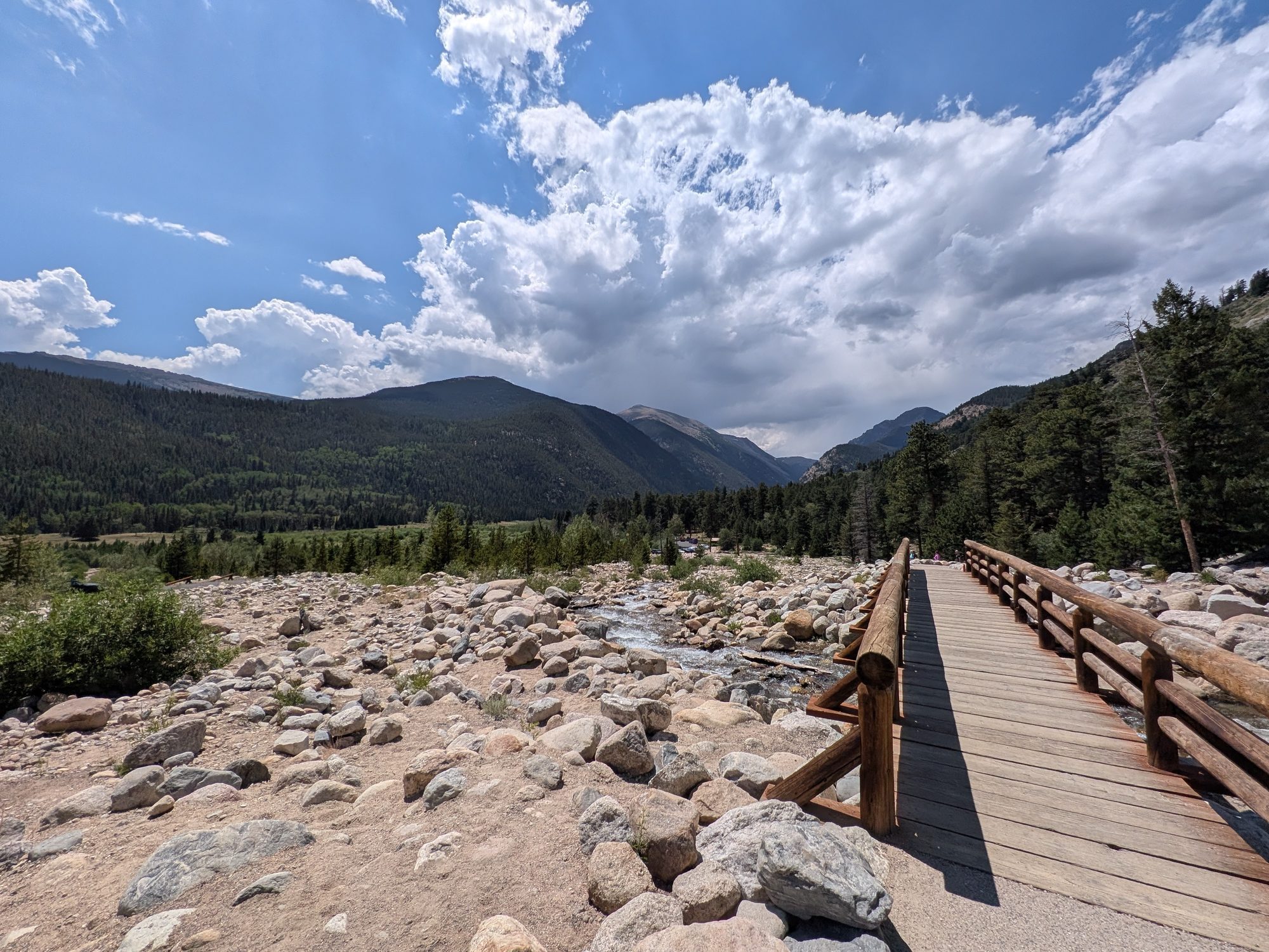 Wooden footbridge on the Alluvial Fan Trail with mountains and clouds behind