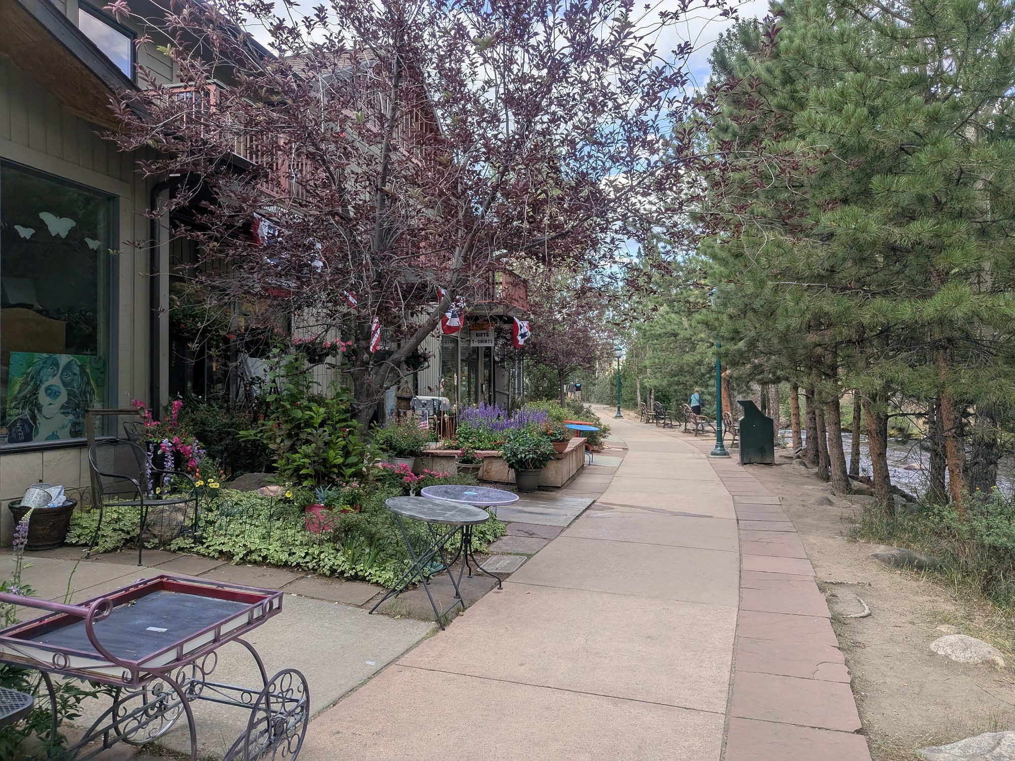 Paved Estes Park Riverwalk path lined with flowers, shops, and trees