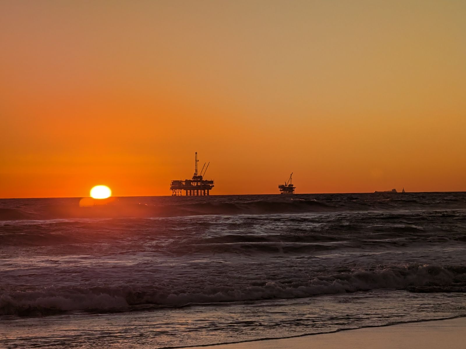 Sun dipping toward the ocean behind an oil platform at Huntington Beach