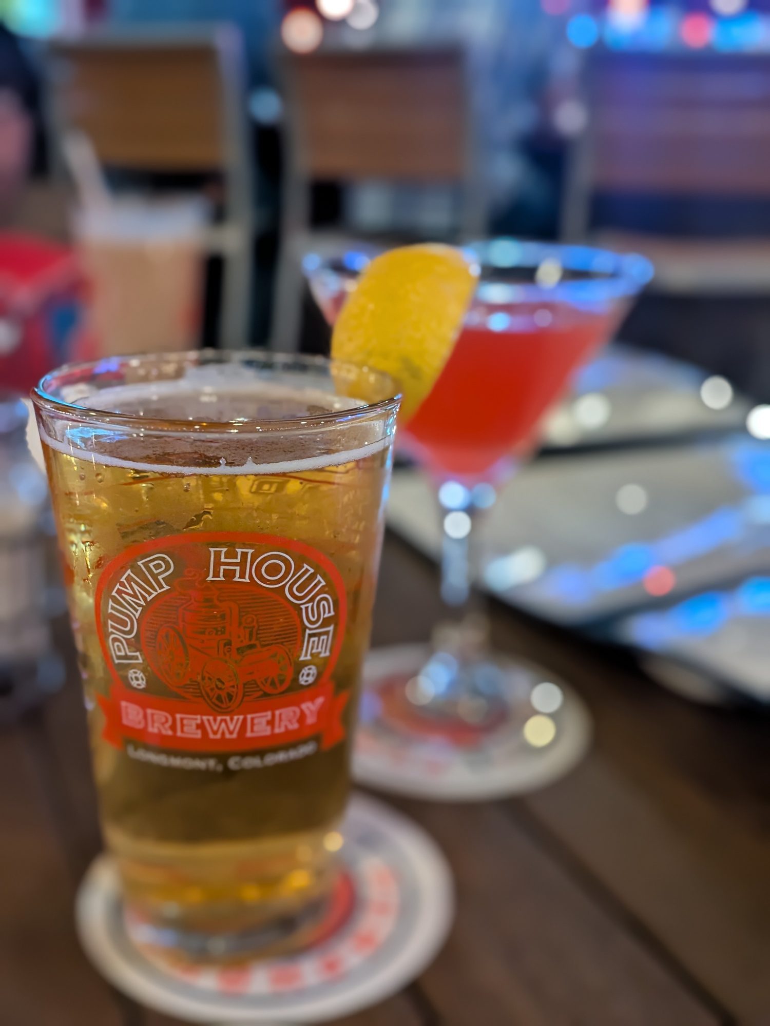 Pint of house beer in a Pumphouse Brewery Longmont glass with a cocktail behind it
