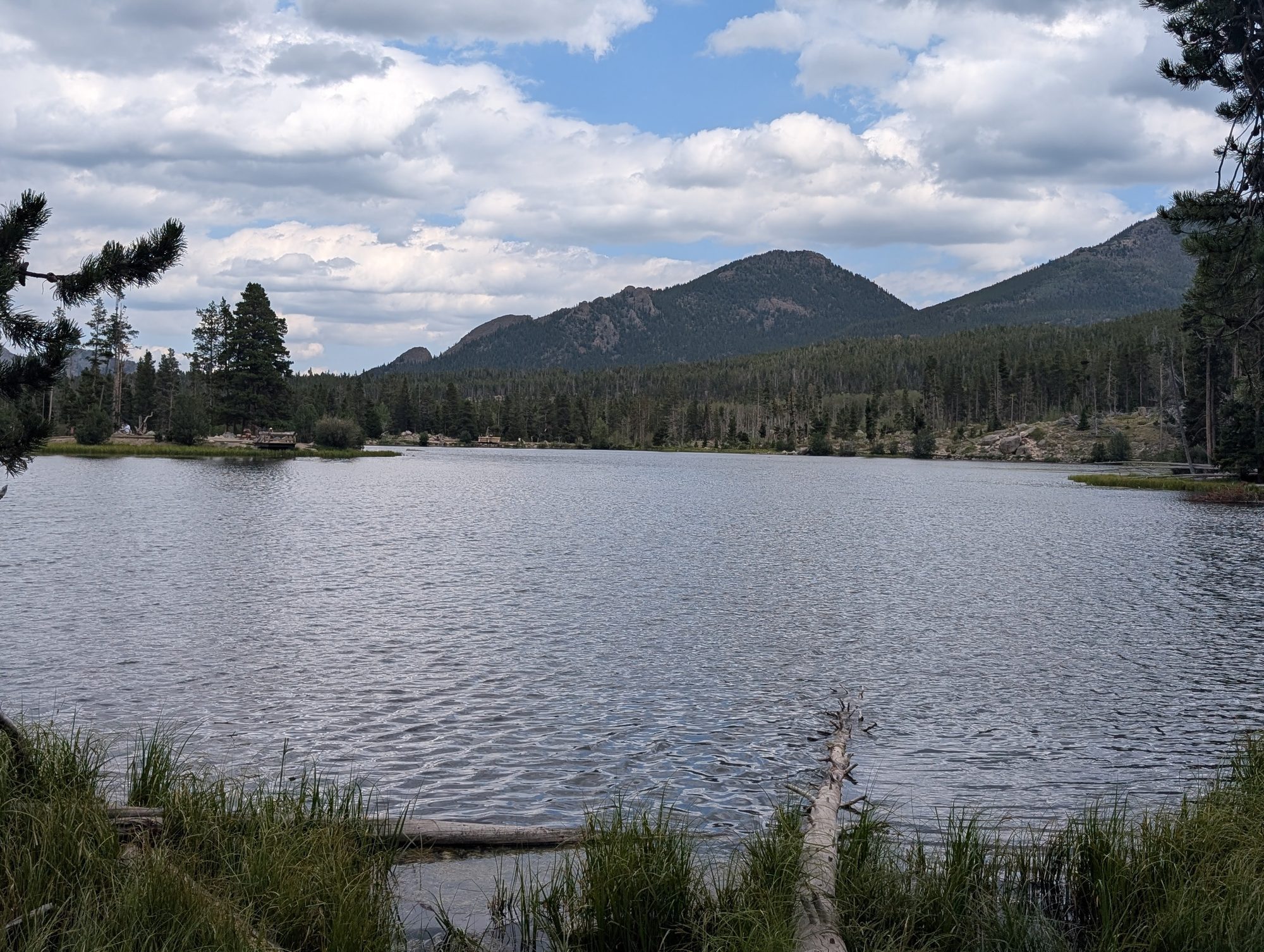 Sprague Lake with calm water and mountains behind on a partly cloudy day